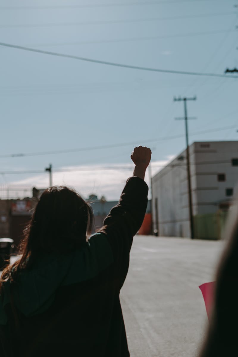 Silhouette of people protesting with raised fists in an urban street setting.