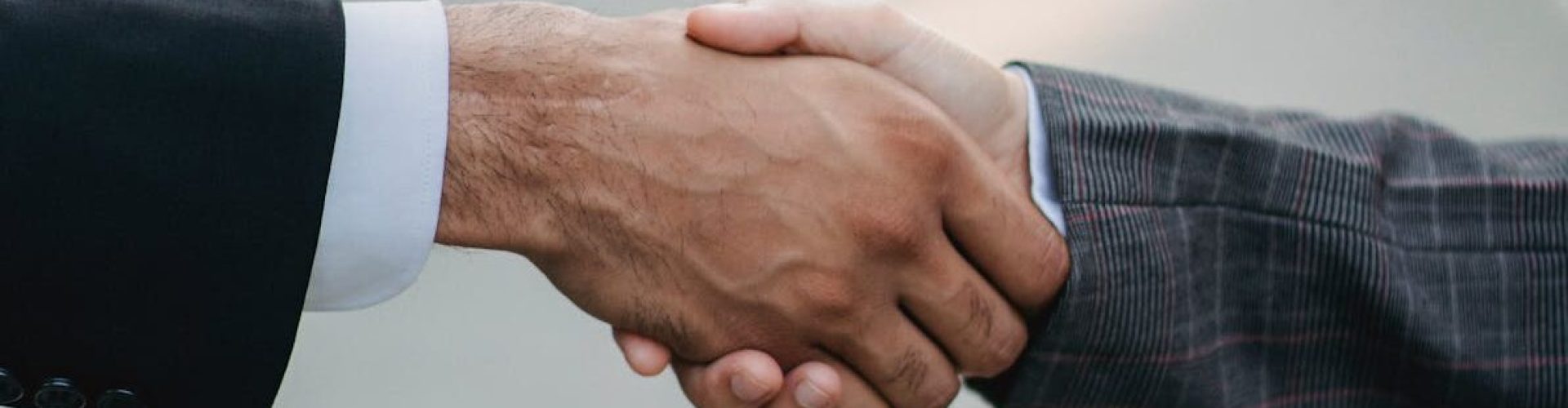 pexels-photo-4963445-4963445 Two businessmen shaking hands outside, symbolizing cooperation and agreement in a city setting.